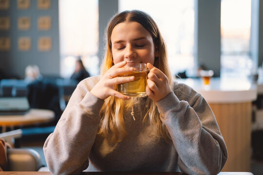 Portrait of a joyful teengirl enjoying a cup of tea at cafe. Smiling beautiful girl drinks hot tea in winter. Teengirl drinking hot tea. Cafe city lifestyle. Colorful portrait of happy pretty girl