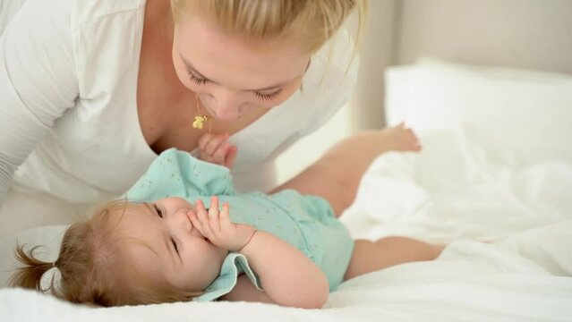 Mother plays tickle her baby girl in bed in morning. Family grows child in love, tender and care. Happy parent and child spent time together. Maternity leave