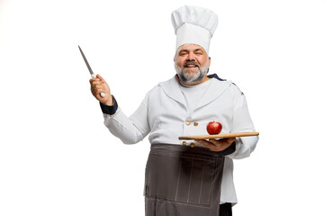 Portrait of cheerful bearded man, restaurant chef in uniform with knife and tomato on cutting board isolated on white background