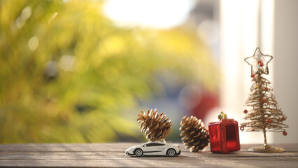 pine cones on miniature car and Christmas tree decorations on wooden table with nature outdoor view