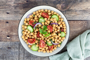 Obraz na płótnie Canvas Chickpea salad with tomatoes, cucumbers, onions and olive oil on a wooden background. High protein salad. Top view. Selective focus. Oriental and Mediterranean cuisine. 