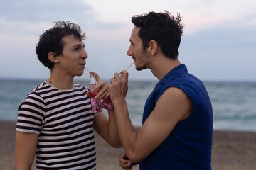 Happy young couple enjoy at the beach. Men drinking juice. LGBT community..