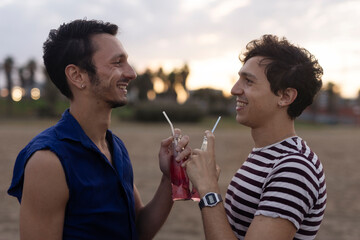 Fototapeta premium Happy young couple enjoy at the beach. Men drinking juice. LGBT community..