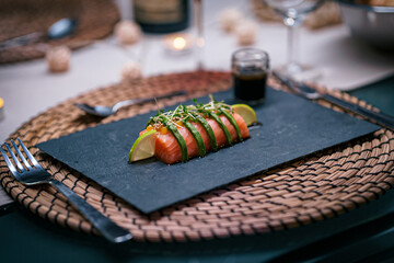 Repas composé d'une assiette de sashimi de saumon, avec avocats, dressé sur une assiette en ardoise