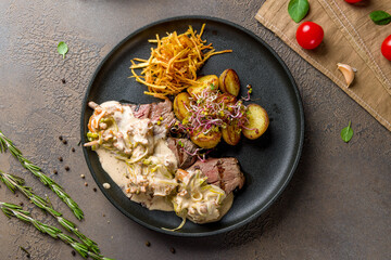 medallions of beef with creamy sauce and mushrooms on black plate top view