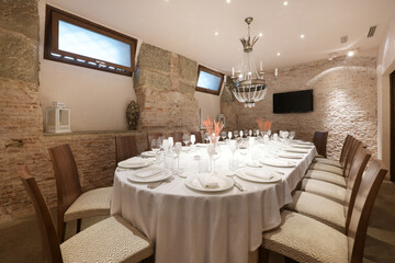 Dining table of a restaurant with service set with glasses and plates and an ornamental lamp on the ceiling