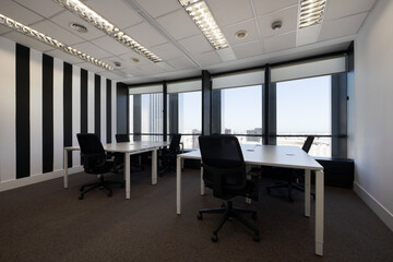Several empty corporate work desks with large windows overlooking the city