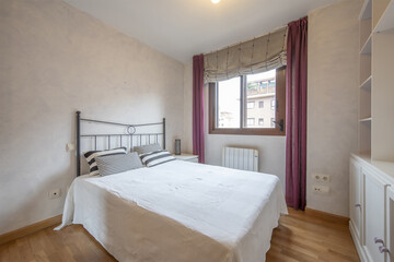 Fototapeta na wymiar A double room with a double bed with a white wooden bookcase and a window with purple curtains and curtains