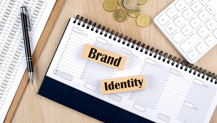 BRAND IDENTITY word written on wooden block on planner with coins, clipboard and a calculator