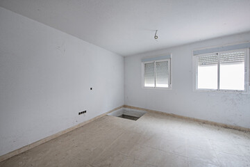 A room with aluminum windows and a hole in the floor that must be finished to finish the electrical...