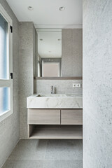 Toilet with light colored marble tiles, veined marble cabinet and low wooden drawers