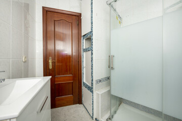 Bathroom with a small white porcelain sink with a shower cabin with translucent glass sliding doors...
