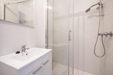 Small bathroom with white lacquered wood cabinets with doors, frameless mirror on the wall,...