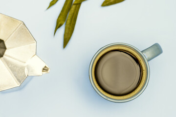 Still life with espresso coffee in a small blue porcelain cup, iron coffee pot and plain blue background