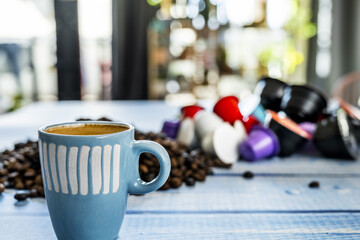 Coffee still life with a blue porcelain cup with assorted capsules and blurred coffee beans
