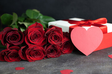 Romantic background for valentine's day or birthday. Red roses, paper hearts and a gift box on a dark background. Valentine's day concept.