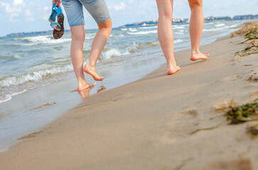 Legs of girls walking on the sand of the sea beach.
