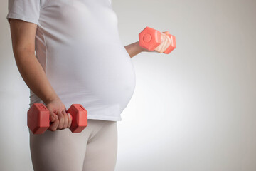 Pregnant girl with a big belly and dumbbells on a white background. The concept of stretching and...