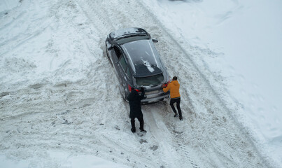 Two men push out a car stuck in the snow. The car skids in a snowdrift on an icy road. Uncleaned roads from snow. Copy space for text