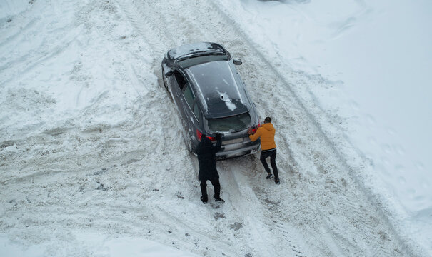 Two men push out a car stuck in the snow. The car skids in a snowdrift on an icy road. Uncleaned roads from snow. Copy space for text
