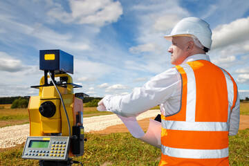 Surveyor in field. Man with geodetic instrument. Road construction. Surveyor with papers looks into...