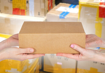 Hands with cardboard box. Parcel without inscriptions. Concept of delivery of goods by mail. Blurred parcel behind box. Box is handed over to customer. Parcel from courier company.