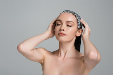 young woman with closed eyes applying mask on wet hair isolated on grey