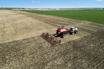 Tractor pulling an air seeder, seeding a field with blue sky in the distance, West of High River; Alberta, Canada