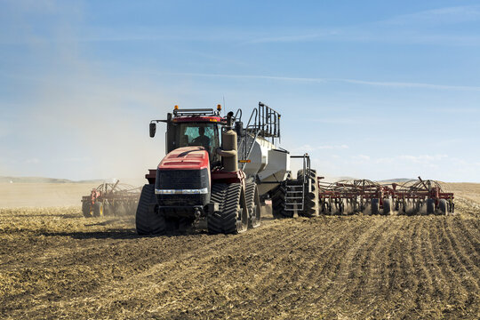 Tractor pulling an air seeder, seeding a field with blue sky and clouds in the background; Rockyford, Alberta, Canada