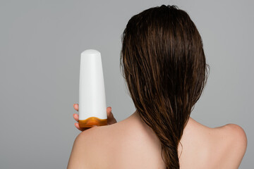 back view of young woman with wet hair and bare shoulders holding bottle with shampoo isolated on...