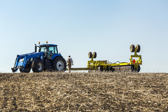 Farmer walking towards tractor with rollers in a canola stubble field with blue sky; Acme, Alberta, Canada