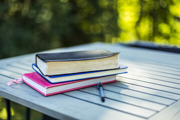 Bible and books piled on a table with a pen outdoors; Surrey, British Columbia, Canada