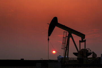 Silhouette of pumpjack with a glowing warm sun ball in the background, West of Airdrie; Alberta, Canada