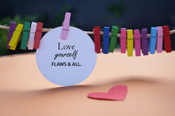 Self love and care concept. Inspirational motivational quote - Love yourself flaws and all. with text message on white circle paper, red heart and colorful wooden clips. Self love and care concept. - obrazy, fototapety, plakaty