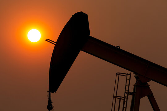 Silhouette of pumpjack with a glowing warm sun ball in the background, West of Airdrie; Alberta, Canada