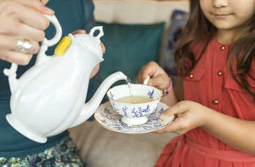 A mother pouring tea into a teacup with saucer for her daughter; Surrey, British Columbia, Canada