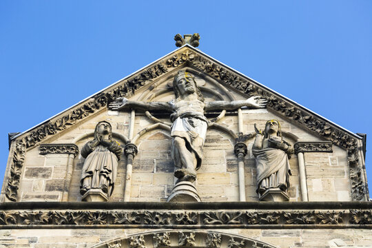 Close-up of crucifix on top of stone church peaked facade with blue sky; Trier, Germany
