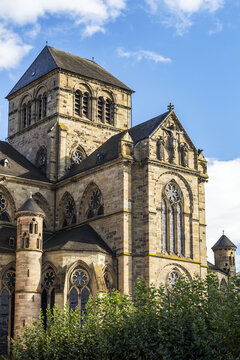 Back side of a large stone church with arched stained glass windows and round turrets with blue sky and clouds; Trier, Germany