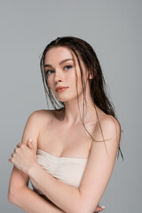 pretty and young woman with wet hair and bare shoulders looking at camera isolated on grey