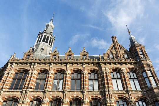 Looking up at colourful building facade with Zuiderkerk church steeple, blue sky and clouds in the background; Amsterdam, Netherlands