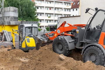 Small loader and excavator digger machine moving heap of earth and debris rubble at construction...