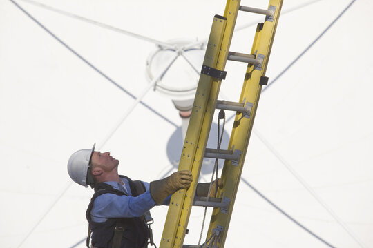 Cable lineman climbing a ladder in front of a satellite dish