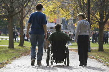 Rear view of a man sitting in a wheelchair with a man and a woman walking to a war protest