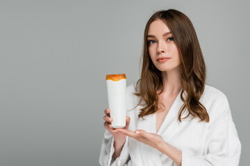 young woman with shiny hair holding bottle with shampoo isolated on grey