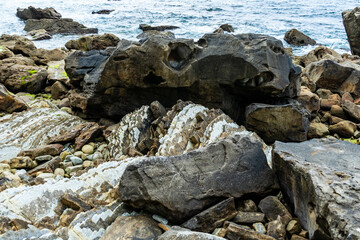 Fototapeta na wymiar Pebbles and boulders on the seashore. Rocky ocean shore.