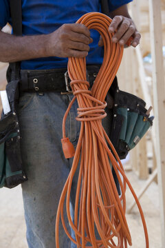 Mid section view of a carpenter holding coiled power cord