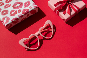 Gift boxes with red bow with heart shaped sunglasses on the red background. Valentine's day concept...