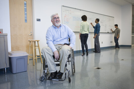 University professor with Muscular Dystrophy in a wheelchair with his students in the background