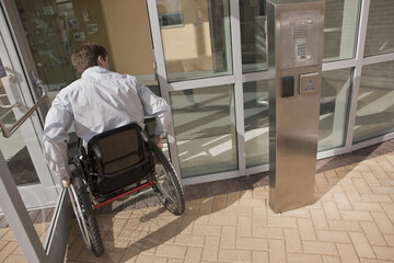 Businessman with spinal cord injury in a wheelchair entering to office building