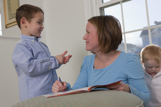 Boy signing the word 'Write' in American Sign Language while communicating with his mother